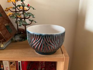 A blue bowl with red-orange organic carvings on its outside. Inside is glazed white, overflowing out over the rim.