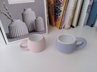 A pink and a blue curvy espresso cup, their glaze just painted on and both with a white inside.
