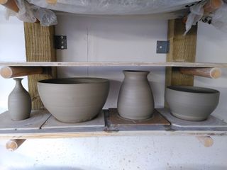 Clay forms drying on their bats after throwing:  small bud vase with a narrow neck and flared rim, a large bowl, a bubbly cone vase with a flared rim and a medium size bowl