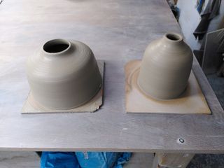 Two clay forms on bats, both with straigh-ish walls curving into a small neck. Left one is flatter while the right one is taller.