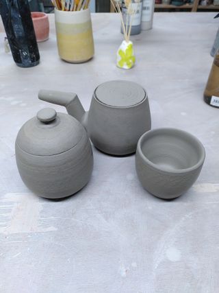 A bulbous teapot with an angular spout, an ovoid jar an a small cup.
