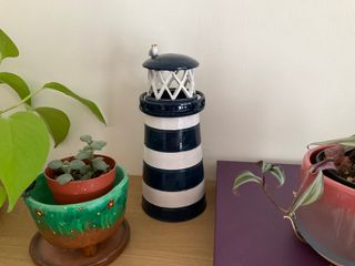 A blue and white striped lighthouse shaped tealight holder, with a seagull sitting on its roof.