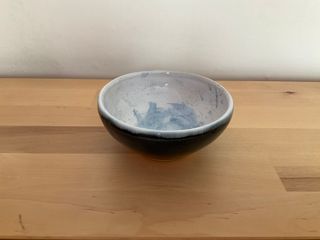 Little bowl lifted by a raw ceramic foot, glazed blue outside and white with blue spots and brush marks inside.