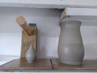 A tiny bulbous bud vase and a regular-size curvy vase drying on a shelf, wet after throwing.