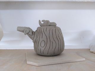 Roughly built clay teapot in the shape of a tree stump, with a beetle as the lid handle and a branch shaped spout.
