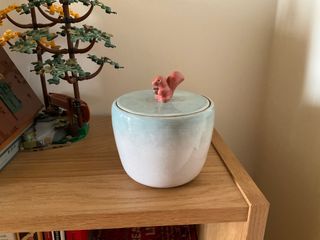 A flat-lidded jar with a knob shaped as a squirrel holding an acorn, glazed in a gradient of light blue on top of a white body.