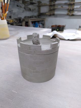 A leather-hard clay jar shaped as a tower with an own sitting on the battlement