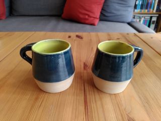 Two angled mugs with their top surface glazed dark blue and inside green, the bottom surface left raw.