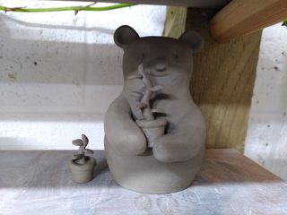 A clay tiny vase shaped as a panda holding a plant in a pot, with a smaller pot next to it.