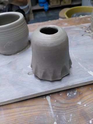 A thrown vase with its bottom carved to resemble a floating sheet.
