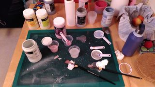 Messy cutting mat with various glaze bottles open, brushes and pots of glaze mixes or water.
