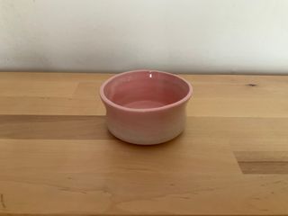 A short cylinder bowl, slightly wonky, glazed pink inside and on the top of the outside.