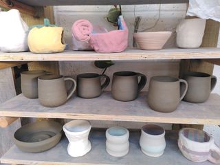 6 mugs with bulbous body and flat handles waiting to dry on a shelf, each not quite the same as the other.