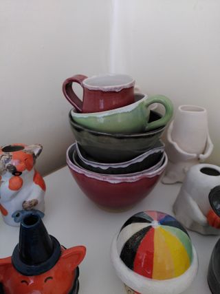 A stack of bowls and cups on top of a shelf, among other smaller ceramics.
