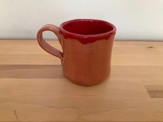 Slab built mug glazed orange on the outside and red inside, dripping out at the top.