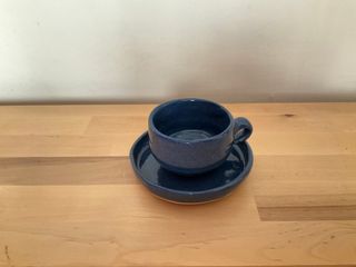 A short but wide coffee cup and a matching saucer, both glazed in a dark, speckled, blue.