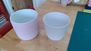 Two planters coated in painted glaze, left one light purple and right one light green, both with white inside overflowing at the rim.
