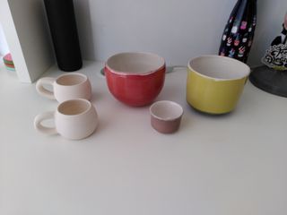 Two bisque fired espresso cups, and three finished pieces: an orange curvy planter, a green straight planter and a purplish grey handle-free cup (all white inside).
