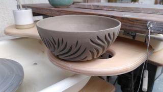 A leather hard clay bowl with organic carvings on its side.