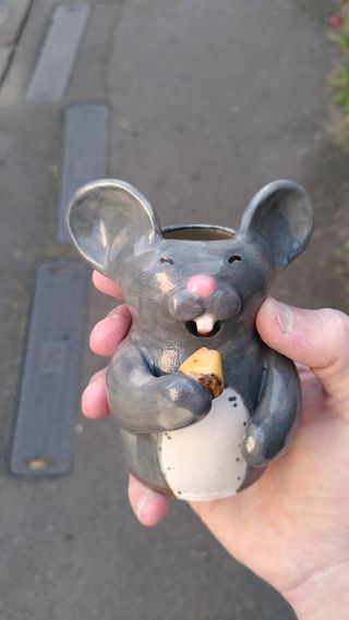 Hand-size vase shaped as a grey mouse about to take a bite in a piece of cheese.
