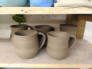5 mugs, trimmed and with their handles, drying on a shelf
