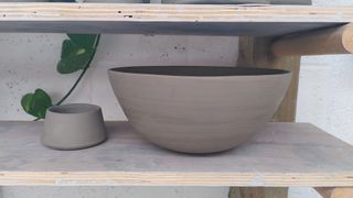 A large trimmed clay bowl on a shelf, next to a tinier conic form.