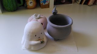 Clay pots painted in glaze: a little ghost sipping tea in a green mug, a crow sitting on the rim of a cauldron and a carved pumpkin