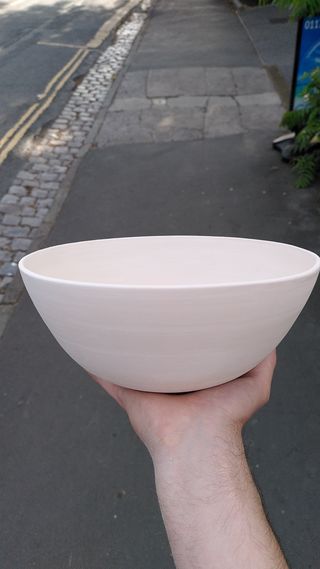 A hand holding a large bisque fired bowl