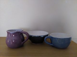 A bubbly purple mug, a dark green bowl and a blue curvy cup, all with white glaze inside overflowing over the top.