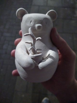 Hand holding a bisque-fired white clay tiny vase shaped as a panda holding a plant in a pot.