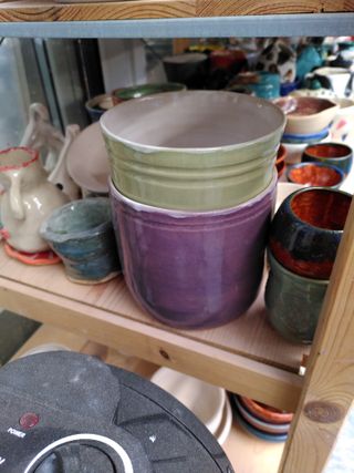 A purple and a green planter on a shelf among other pieces of ceramics.
