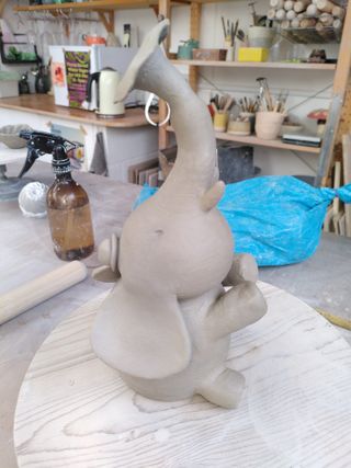 A clay form shaped as an elephant with a bowler hat, sat down throwing water with its trunk.