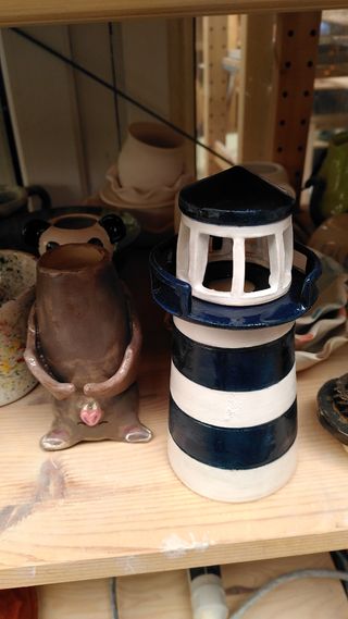 A shelf of finished ceramic pieces, with focus on a bat vase and blue striped lighthouse.
