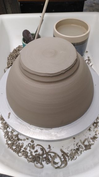 An upside down leather hard clay bowl on a wheel before trimming, its bottom very uneven.