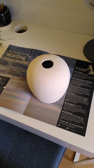 Clay pot painted in light yellow glaze on top of a magazine