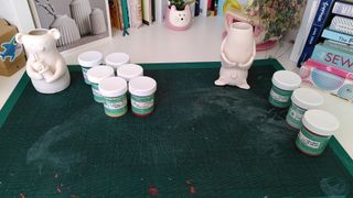 A white bisque fired panda vase and a white bisque fired bat vase on top of a craft mat, with pots of underglaze lined up next to them.
