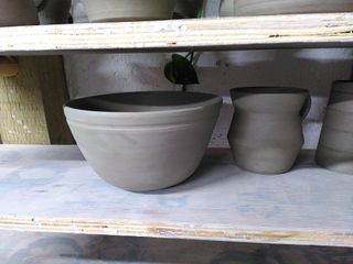 Trimmed curvy clay bowl (with a carved stripe towards the rim) and angular clay mug waiting to dry.
