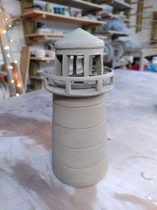 A leather hard clay lighthouse with spaced carved out at its top and on the rail.
