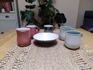 5 mugs and a bowl: 2 light red mugs with a white inside and rim, 2 white mugs with a teal inside and rim, a yellow with sponged blue overlay mug and a bowl with a blend of blue and yellow outside and white inside.