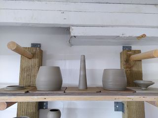 Two bulbous jars, a flat and a coned lid and a tall narrow cone in wet clay on a shelf.
