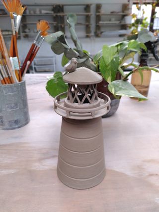 A leather hard clay lighthouse candle holder with diamond opening for the light.
