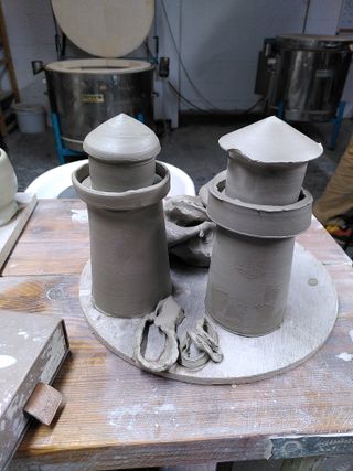 Two lighthouses throwing in grey clay standing on a bat alongside flopped pieces.
