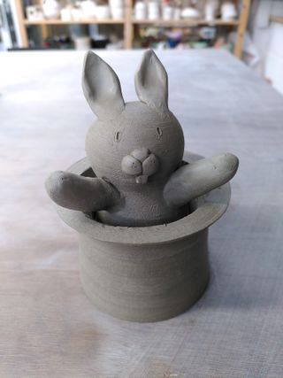 A clay sculpture of a rabbit popping its head out of an upside-down top hat.
