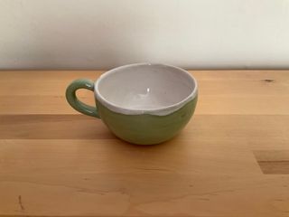 A flat and wide cup, glazed in a light green outside and white inside.