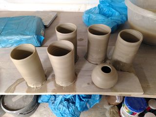 5 clay cylinders and a little ball shaped vase on a plank after throwing.
