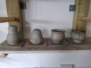 4 clay thrown forms on a shelf: a vase shaped like a body, a ghost, a cauldron body and a pumpkin.