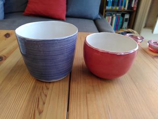 A purple planter and a dark orange one sitting on a wooden table.
