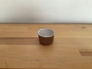 A tiny cup or tea candle holder, glazed in light warm grey outside with a white inside.