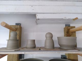 Thrown clay forms waiting to dry on their bats (left to right): a hat with some double gourd popping out of it, a volcano-like cup, a body and head closed form and a flared bowl.