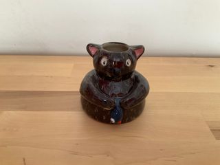 Little vase in the shape of a brown cat holding a blue fish (tongue out, dead eye).